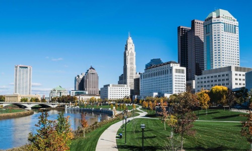 a park with a river and tall buildings in the background