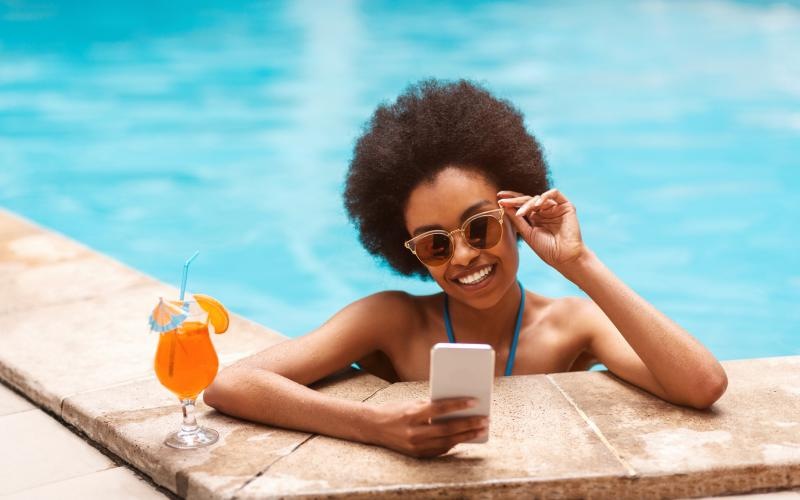 a person in sunglasses and a garment sitting by a pool with a drink