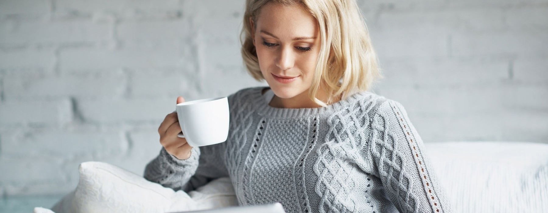 a woman sitting on a couch looking at a tablet holding a mug