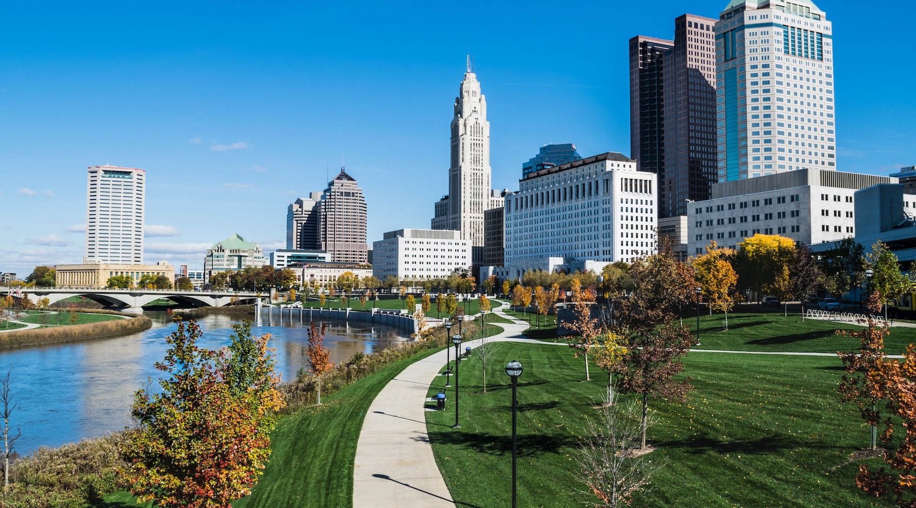 a park with walkway river next to a downtown area