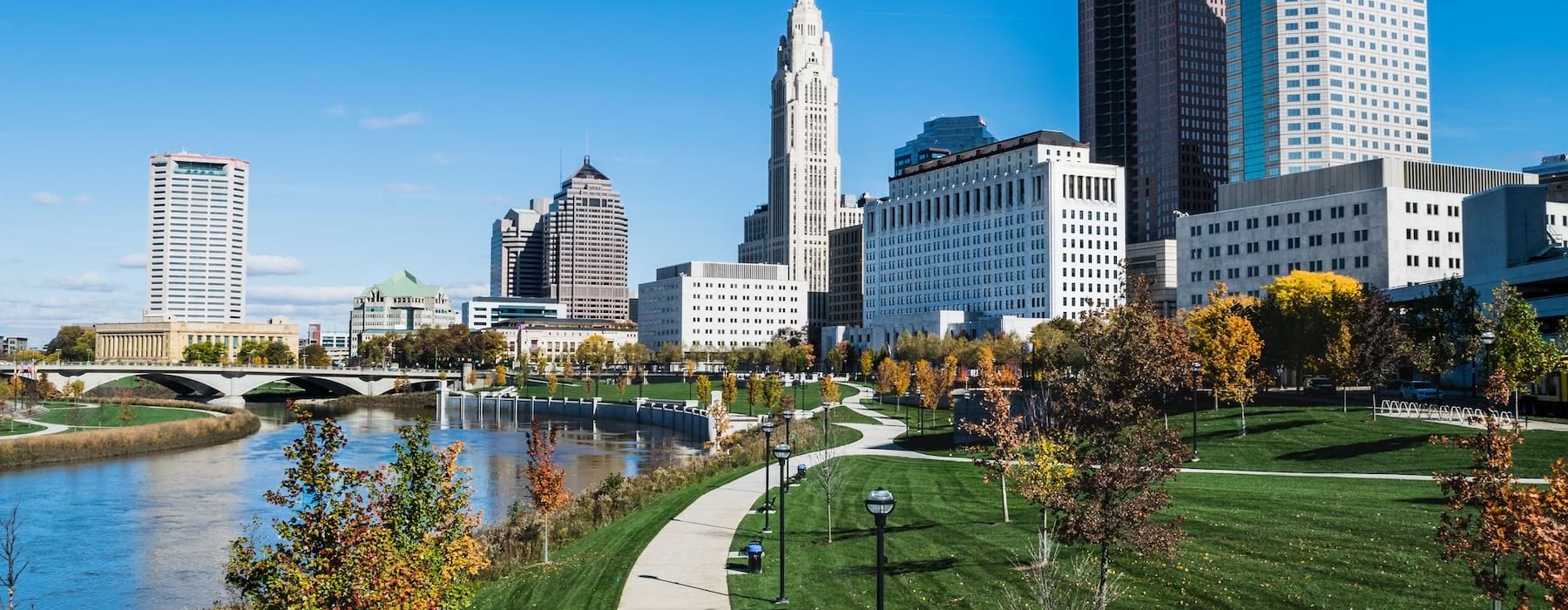a park with walkway river next to a downtown area